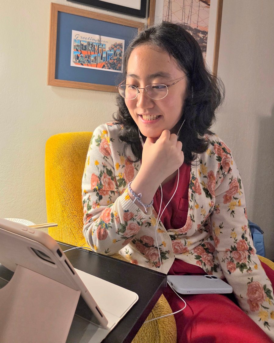 Me smiling at my tablet in a floral cardigan, sitting in a yellow armchair